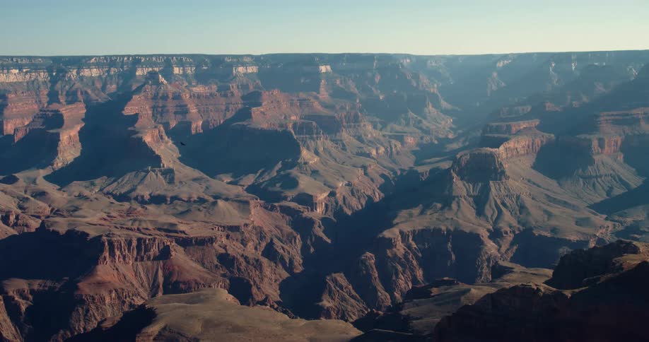 The sun shines brightly upon rock formations and mountains under a clear sky