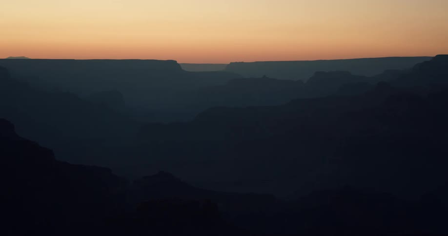 Silhouettes of rock formations and mountains in a hazy orange sky