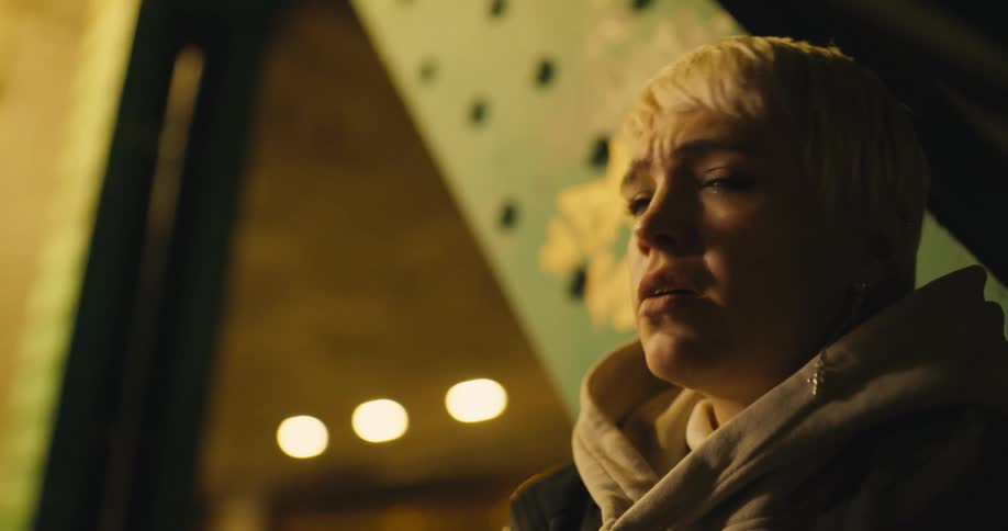 A woman looks around nervously as she stands against a bridge