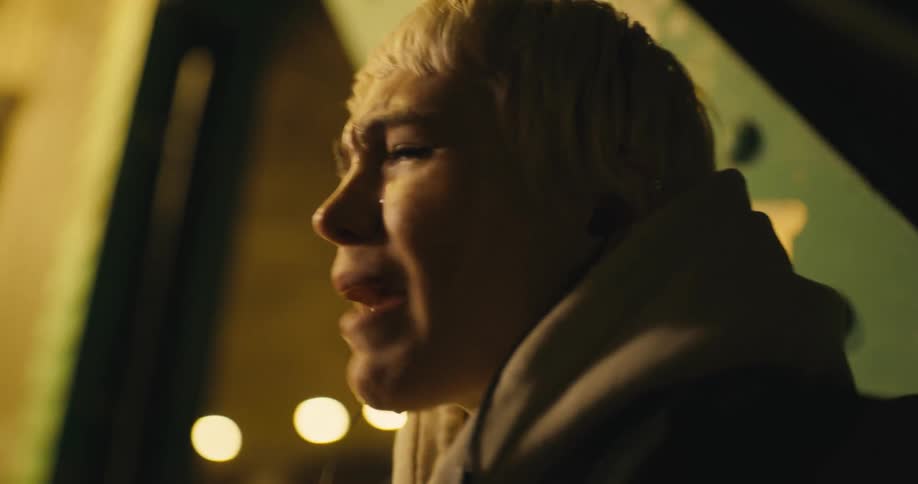 Young white woman sitting outdoors wearing earphones and shouting and crying while video calling someone on her smartphone