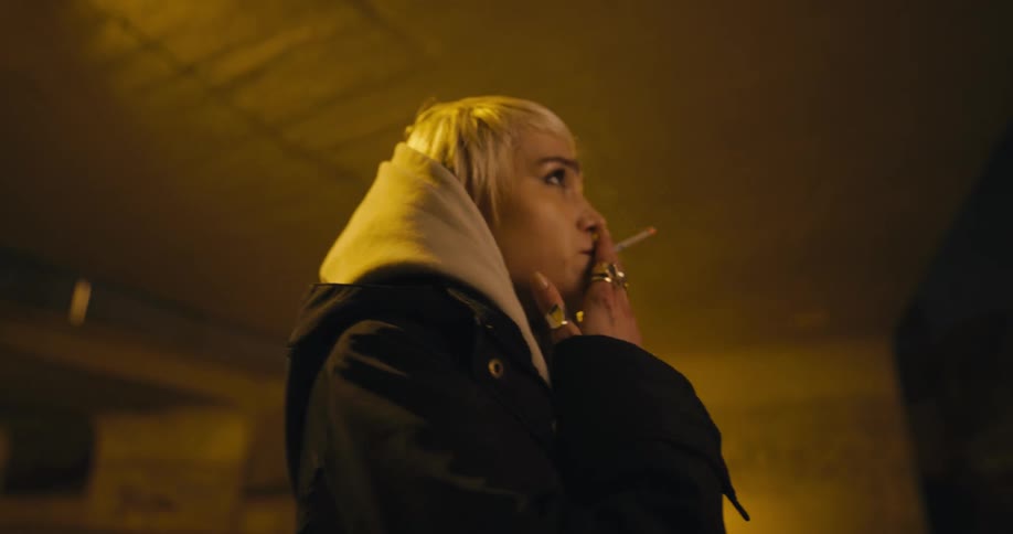 At night woman stands under concrete bridge near busy street smoking and looking around