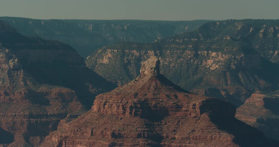 The sun shines brightly upon rock formations and mountains under a hazy sky