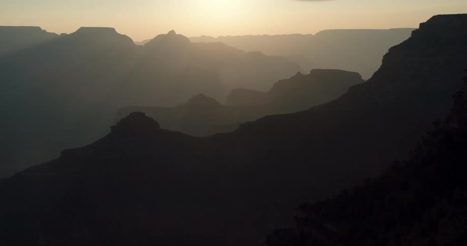 A bright sun in a hazy orange sky is above the silhouette of a mountain range