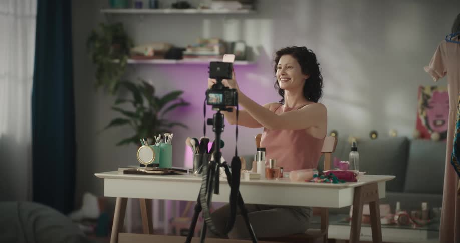 A woman sits at home and video chats on her cell phone in front of a camera she has set up