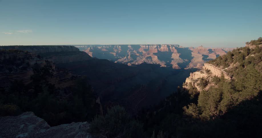 The sun shines brightly on rock formations and forested mountains