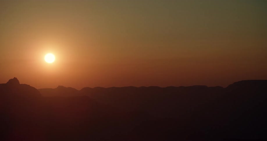 A bright sun in an orange sky is above the silhouette of a mountain range