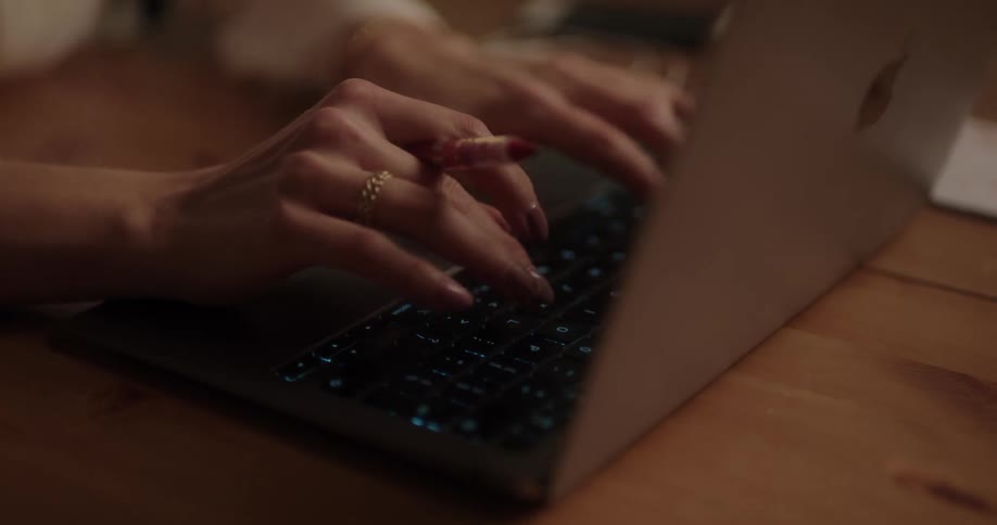 A woman holds a pen in her fingers as she types on a laptop