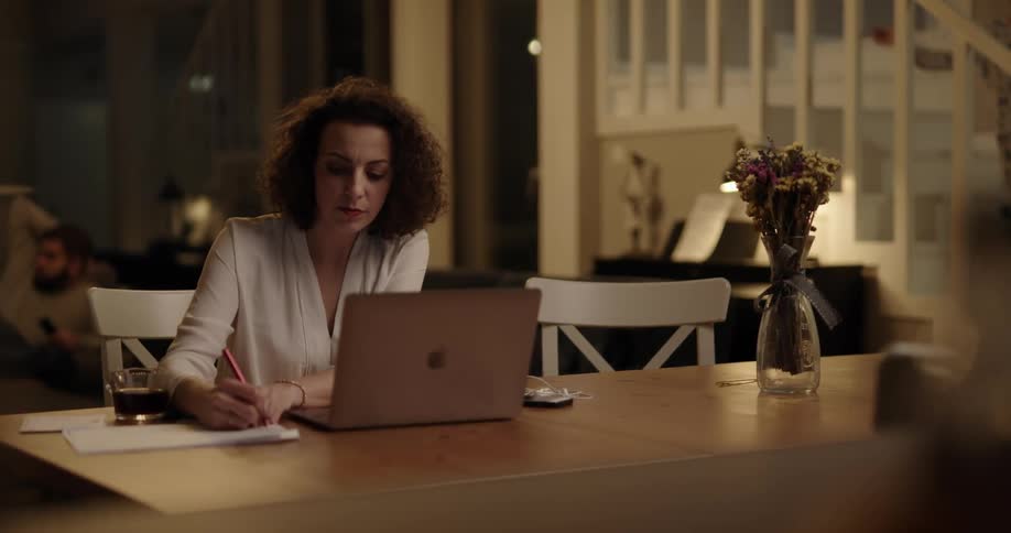 Boy wearing pajamas walks down the stairs at home interrupts his mother working on a laptop