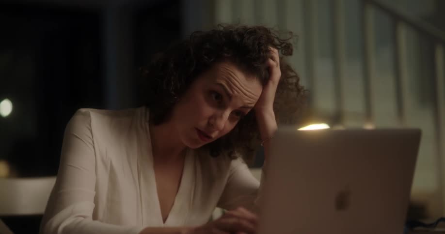 A woman is sitting indoors on a laptop