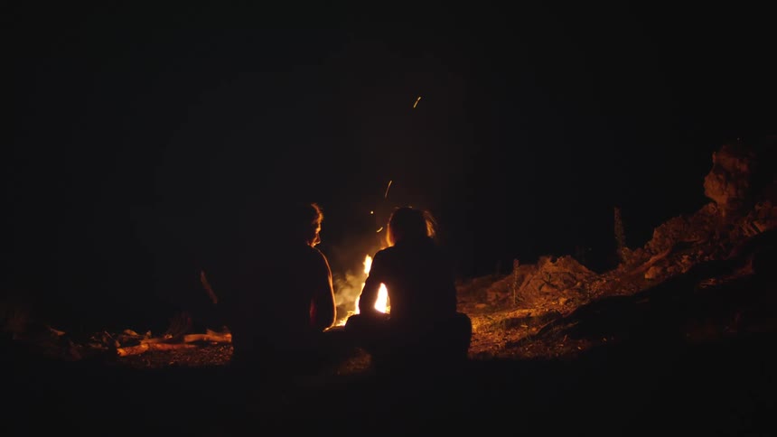 Two women sit by the campfire at night