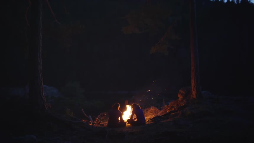 Silhouette of a couple sitting in front of a campfire in the forest at night