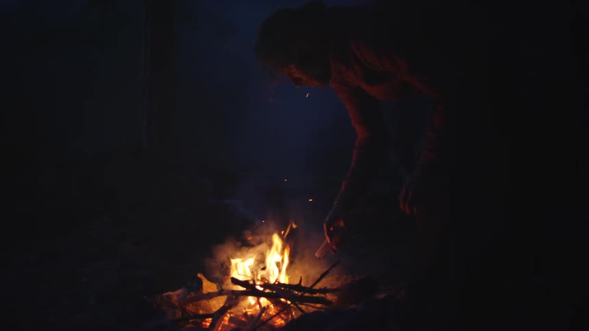 Man adds sticks to a burning campfire at night