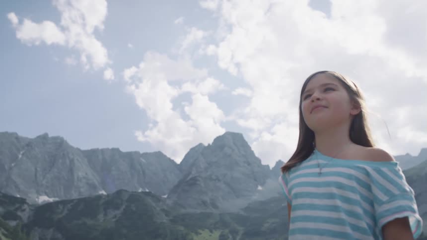 Girl standing outdoors in front of a landscape full of mountains on a sunny day