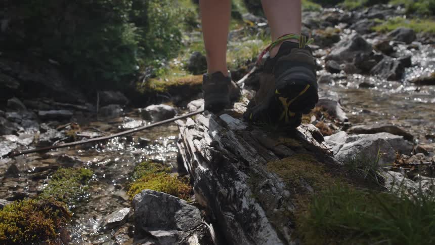Person walking over a log on a shallow river in the mountains while hiking