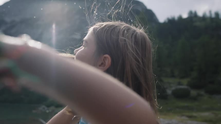 Young girl in a striped shirt throws a stone into a lake near the mountains