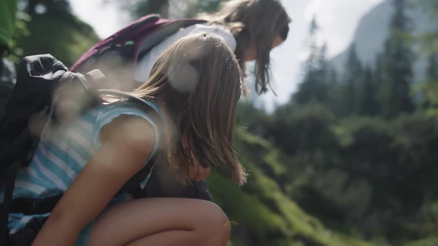 Two girls kneel down on the hill as they hike
