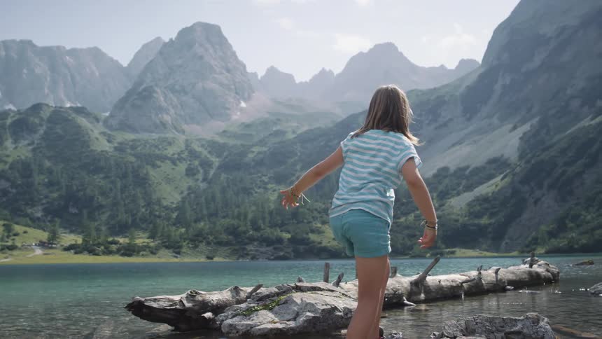 A girl walks across a tree trunk like a balance beam along a lake