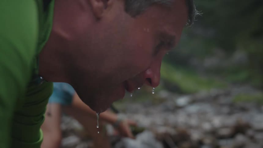 Man picks up water from a river with his hands to wash his face in the mountains at morning