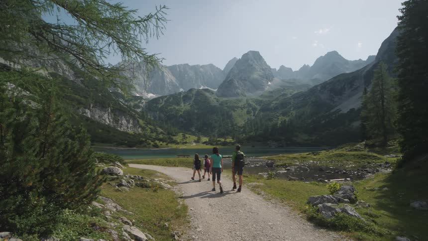 Family of four hiking on a trail through the mountains near a lake in the morning