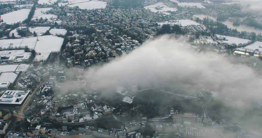 A cloud floats over a town in a valley with snow covered fields trees and ponds