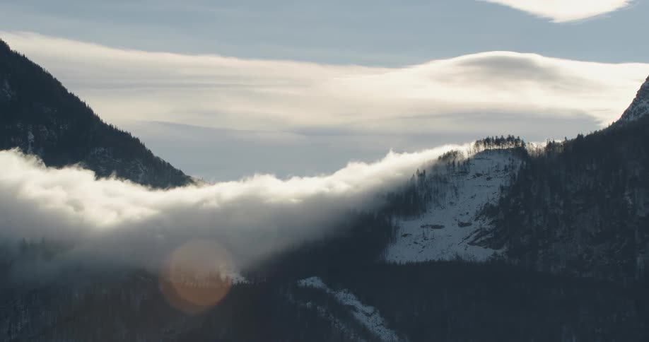 Snow covered forested mountains are high in the clouds