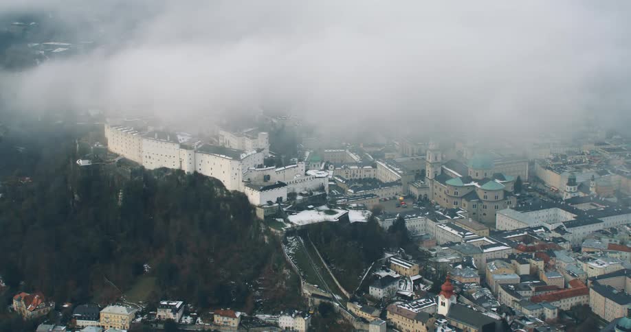 Aerial view of a castle atop a mountain in the middle of the city under the clouds