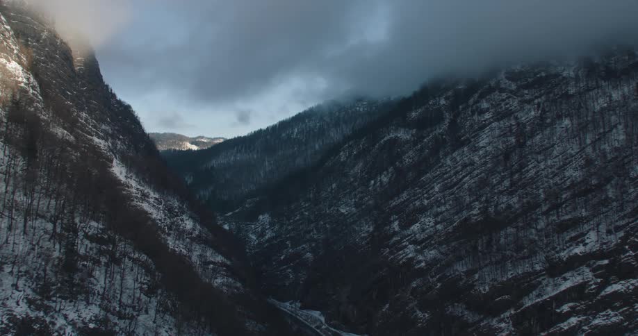 Snow covered forested mountains and a valley below with mountains in the distance