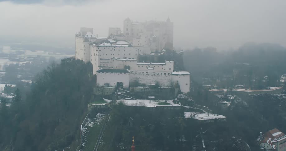 Aerial view of a white castle over a mountain under the clouds