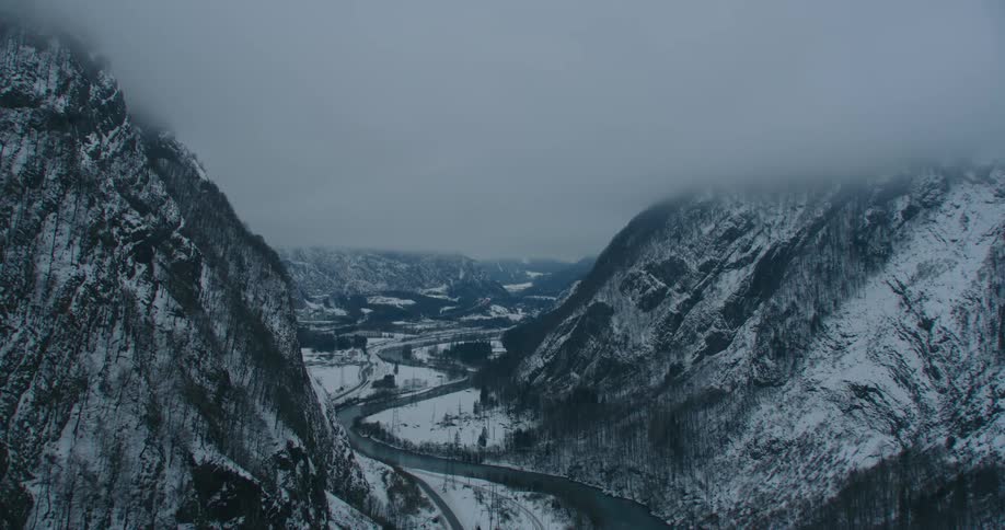 Aerial view of a road on the bottom of a canyon in the mountain next to a river under the clouds