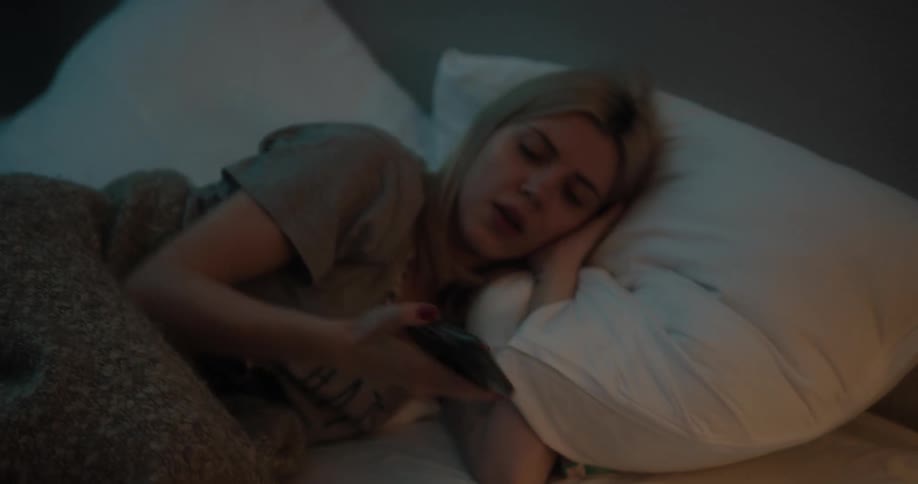 Blond teenaged girl lays in bed then turns on the light and looks at her cellphone