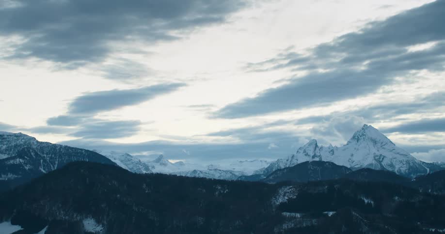 Snow covered mountains and tree lined mountains sit under a cloudy sky