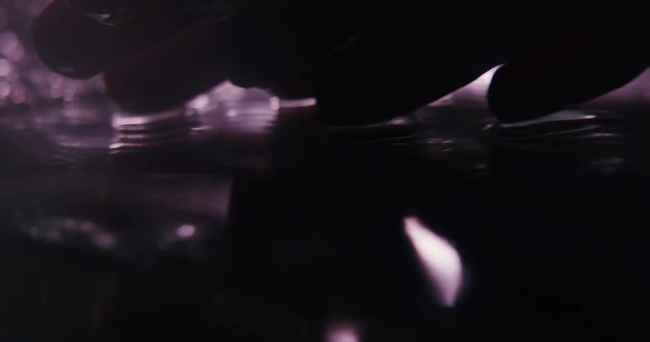 Fingers rubbing the a wet concrete surface under purple lights at night