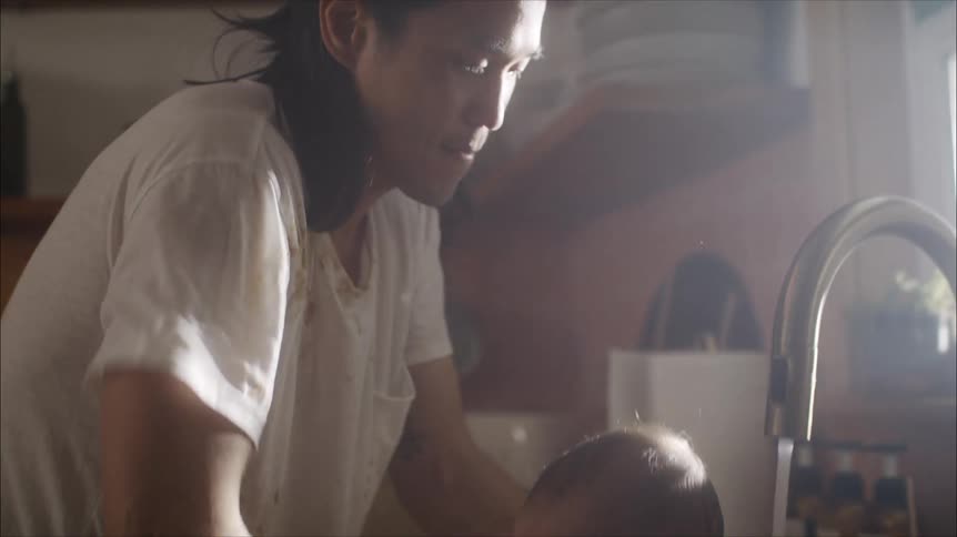 A father bathing his infant child in a kitchen sink on a sunny day