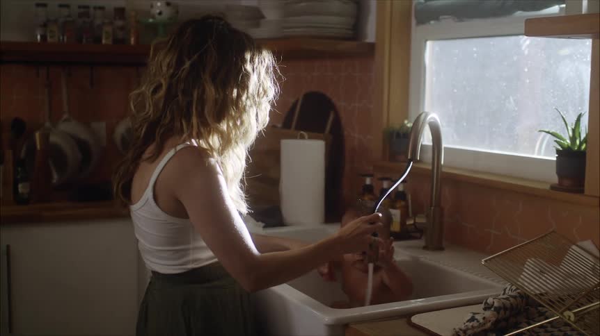 A mother bathing her infant in a white porcelain kitchen sink