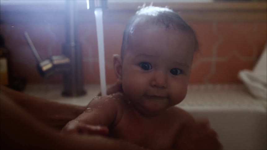 A person washing their baby in a sink