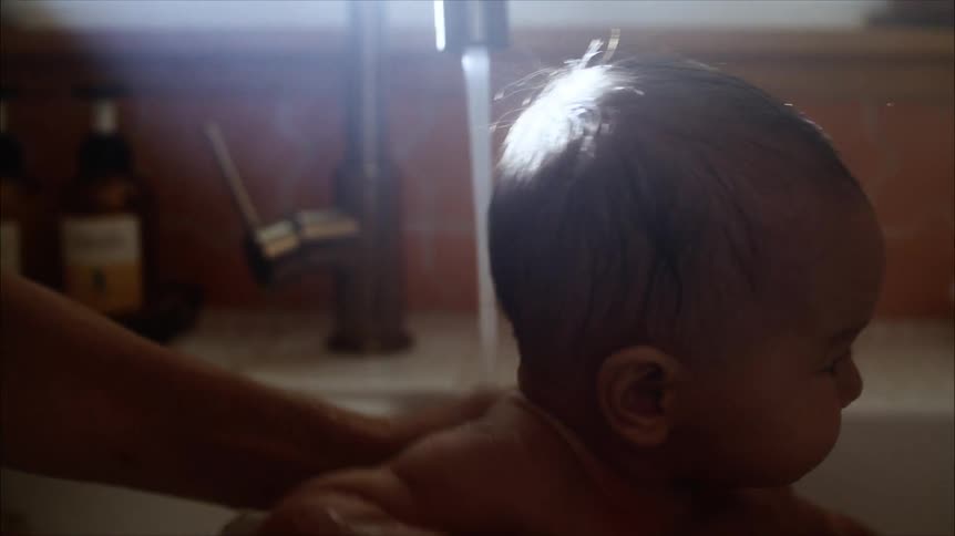 A parent is bathing their infant in a bathtub