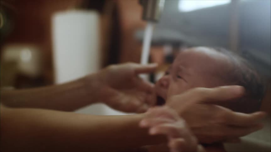 A woman is bathing a baby in a kitchen sink in the daytime