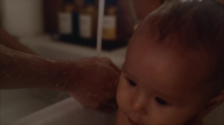 A person bathing their baby in a sink