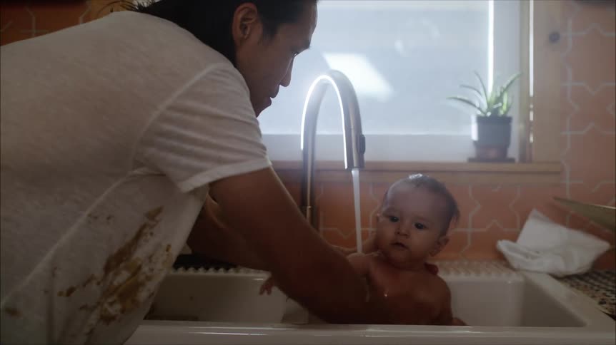 An adult washes a baby in a large sink