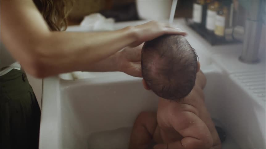 A mother bathing her baby in a sink