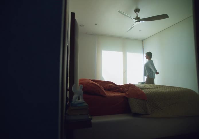 A woman walks into a bedroom in the daytime heading toward the bathroom