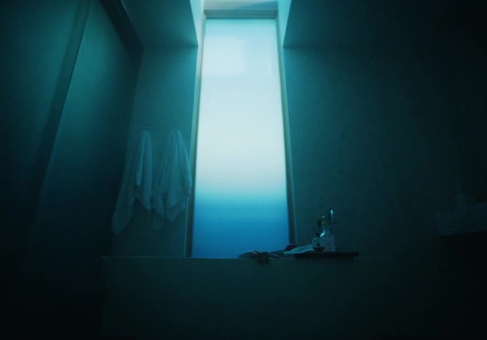 Eerie footage of a man submerging on a bathtub inside a dimly lit bathroom under a skylight