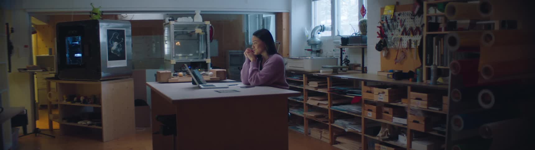 A woman is sitting at a table with a laptop while thinking in a design studio during the daytime