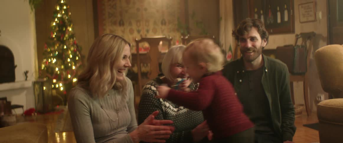 A young boy dances and spins in a circle and falls in to his mothers lap as his grandma and dad clap and dance