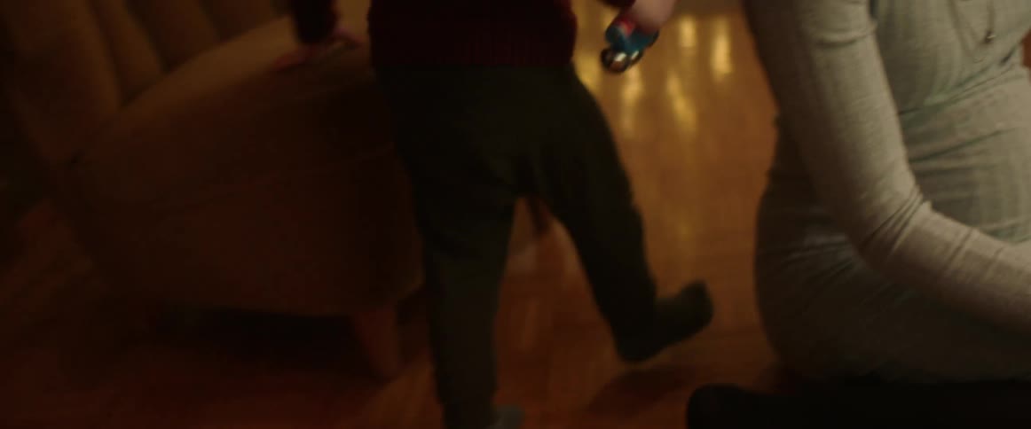 A little boy runs around his pregnant mother who is sitting on the floor with grandma and dad