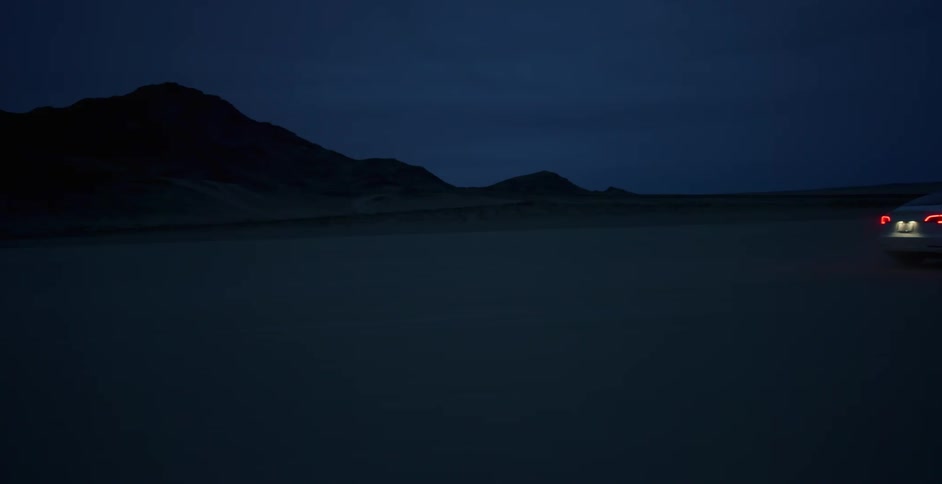 A car travels offroad through an arid flatland at night