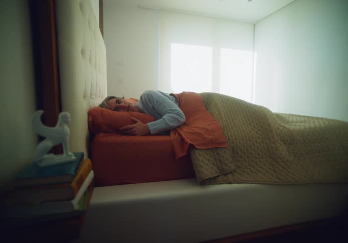 A woman is asleep in bed and then awakens to roll onto her back and stare at the ceiling in the daytime