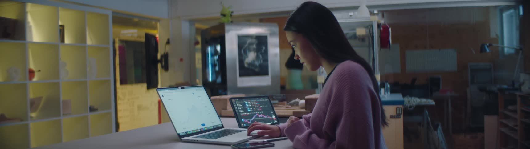 A woman sits at a desk in an office and uses an laptop