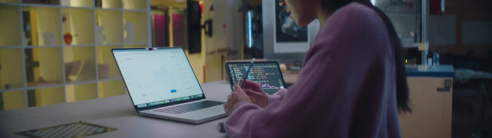 A teenage girl is sitting at a desk working on a laptop computer and there is a tablet computer on the table next to her laptop