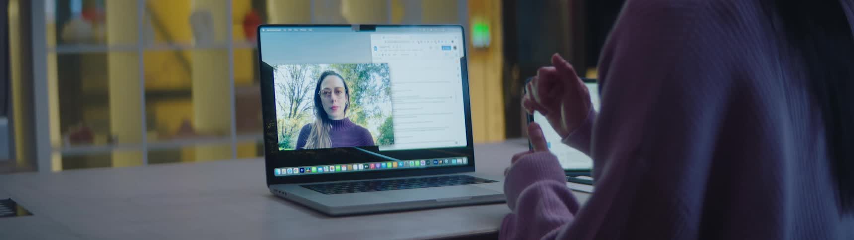A woman in an office video chats with a coworker on a laptop